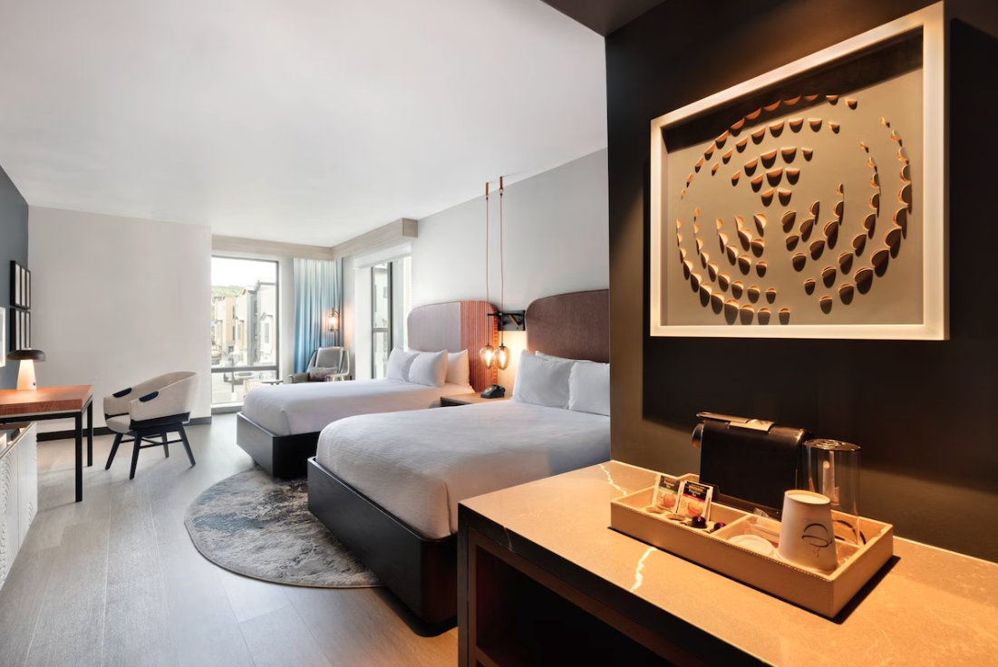 Modern hotel room at Hotel Indigo Silverthorne with two beds, a sitting area, and mountain views, featuring stylish decor and lighting.
